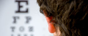 An image of a male's head with an vision chart on the wall in front of him. 