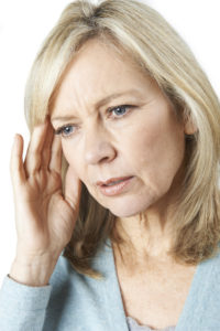 An image of a senior woman holding fingers to the side of her head in confusion.