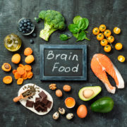 An image of salmon, avocado, dark chocolate, blueberries, and other foods with a small chalkboard that reads: brain foods.