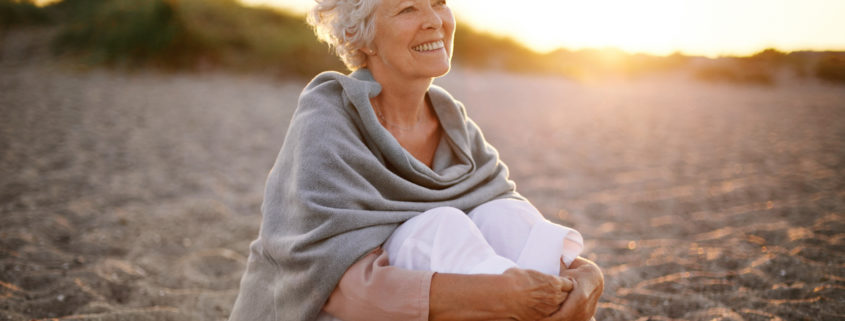 An image of an attractive mature woman sitting on a beach.