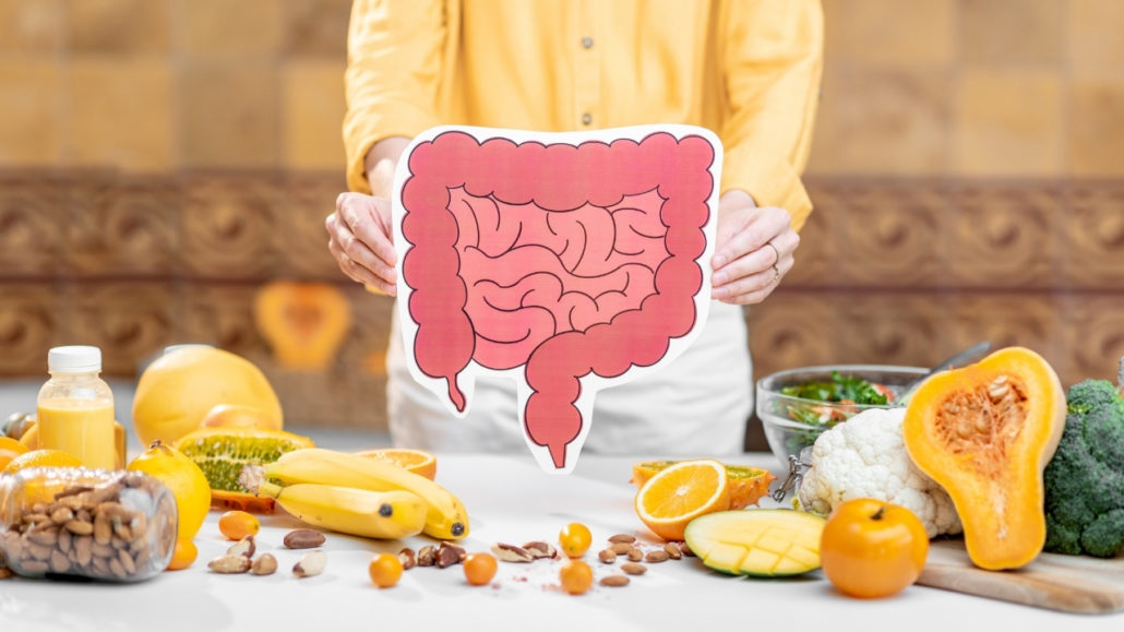 An image of a woman holding a picture of human intestines with a variety of fresh whole-foods on the table.