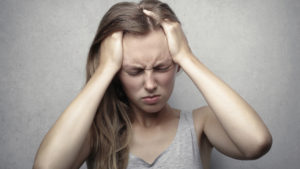 An image of an overwhelmed woman holding her head, eyes tightly closed. 