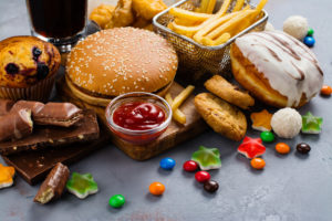 An image of an assortment of unhealthy foods, including donuts, French fries, fried chicken, and soda.