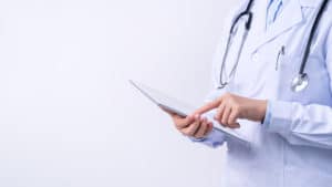 An image of doctor with stethoscope reading a patient's chart. 