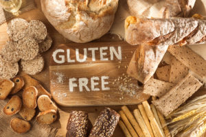 An image of gluten-free pastas, breads, and snacks around a wooden sign that reads, "gluten free."