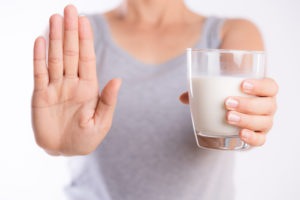 An image of a woman holding a glass of milk in one hand, and holding her other hand out like a stop sign.