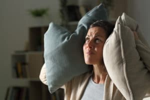 An image of an annoyed woman holding pillows to her ears to block out the noise. 