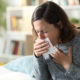 An image of an adult woman coughing into a tissue at home.