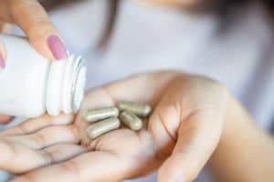 An image of a woman pouring supplement capsules out into her hand. 