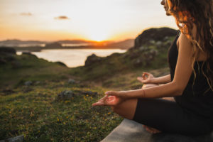 An image of a woman meditating outdoors at sunset.