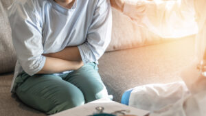 An image of a woman sitting on a sofa holding her stomach in pain.