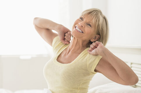 An image of a mature woman stretching in bed after a refreshing night's sleep.