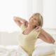 An image of a mature woman stretching in bed after a refreshing night's sleep.